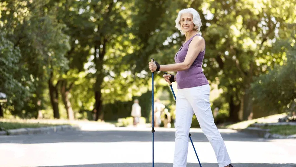 Пожилая женщина, занимающаяся скандинавской ходьбой на улице в солнечный день