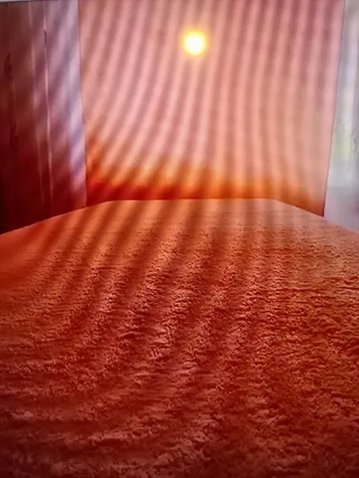 Красный текстиль на кровати с мягкой фактурой на фоне с солнечными лучами, создающими абстрактный узор, освещающий комнату