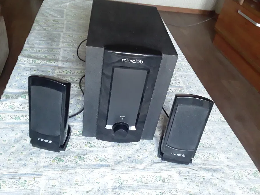 Microlab аудиосистема, екі колонка және сабвуфермен, үстелдің алдында матамен безендірілген.