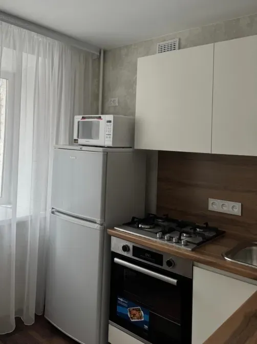 Бұрышта тоңазытқыш, газ плитасы және терезе бар асхана