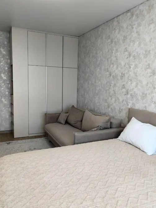 Спальня с двуспальной кроватью и диваном, оформленная в светлых тонах