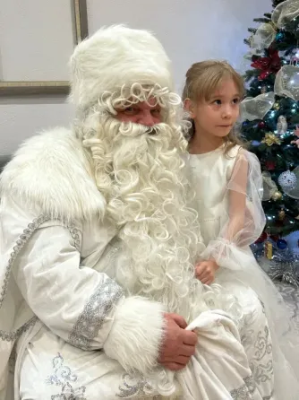 Дед Мороз с девочкой в белом платье на фоне новогодней елки