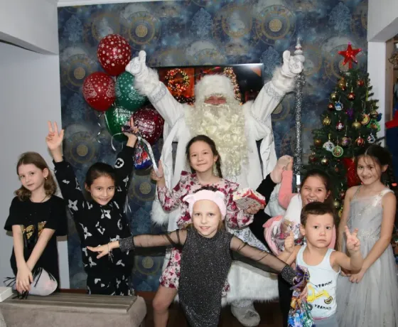 Дед Мороз с девочкой в белом платье на фоне новогодней елки