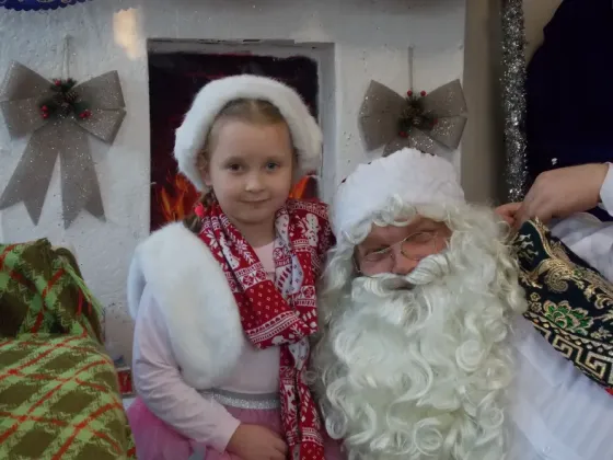 Дед Мороз с девочкой в белом платье на фоне новогодней елки