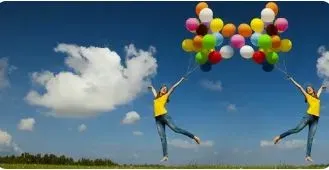 Два человека, стоящие на зеленом поле под голубым небом, держат в руках множество разноцветных шаров, радуясь и прыгая