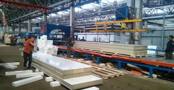 На заводе по производству сэндвич-панелей работники складывают панели в ряд на конвейере