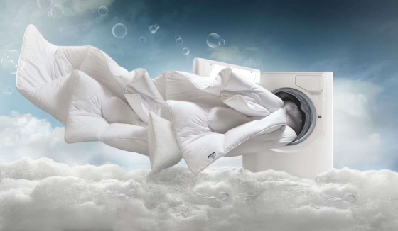 Стиральная машина с расправляющимся пуховым одеялом на фоне облаков и пузырьков