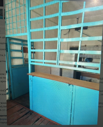 Интерьер комнаты с голубыми стенами и деревянным полом, на заднем плане виден белый холодильник