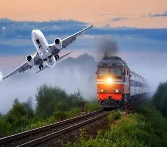 Поезд, движущийся по железной дороге на фоне заката, над которым летит самолет