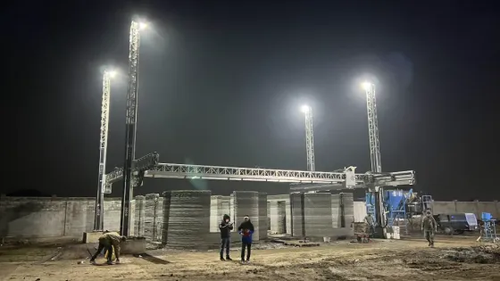 Строительная площадка с 3D-принтером для бетона под вечерним освещением, рабочие и техника на стройке