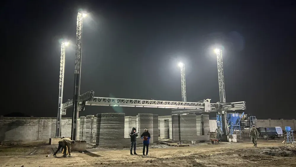 Строительная площадка с 3D-принтером для бетона под вечерним освещением, рабочие и техника на стройке