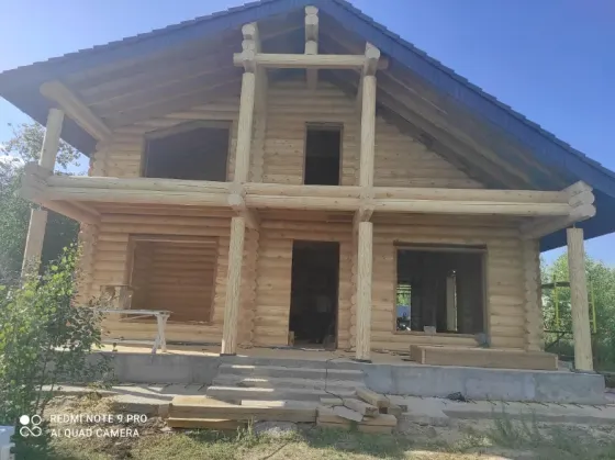 Дом из бревен на стадии строительства с окнами и крышей