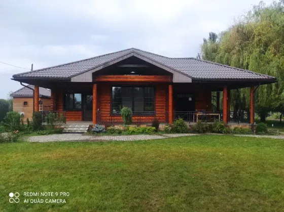 Деревянный дом с большими окнами и крышей из черепицы, окруженный зеленью