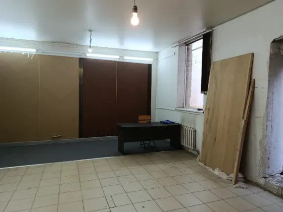 Бос бөлме, қабырғаға ілінген айна мен бұрышта қарапайым үстел