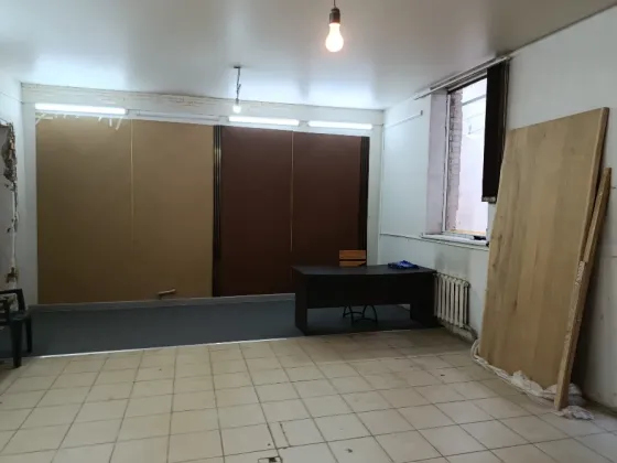 Бос бөлме, қабырғаға ілінген айна мен бұрышта қарапайым үстел