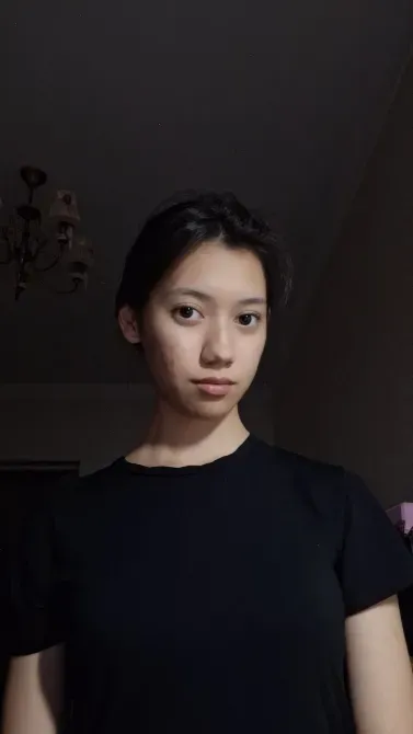 Жас әйелдің портреті, қара киімде, бөлме интерьері фонында поза беріп тұрған.