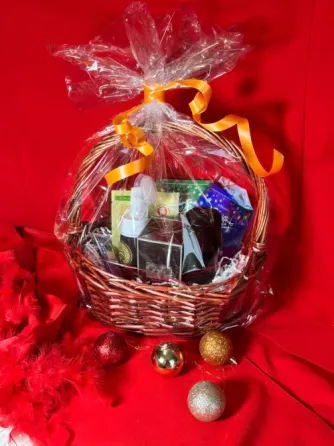 Корзина с подарками, завернутая в прозрачную пленку и перевязанная оранжевой лентой, на красном фоне