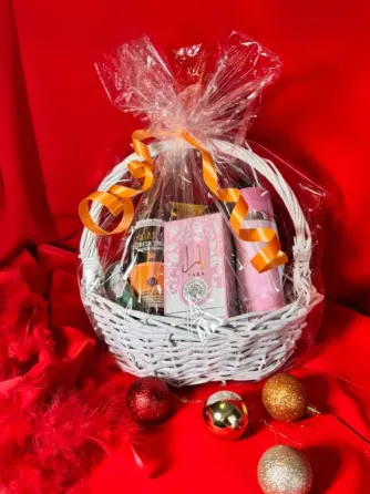 Корзина с подарками, завернутая в прозрачную пленку и перевязанная оранжевой лентой, на красном фоне