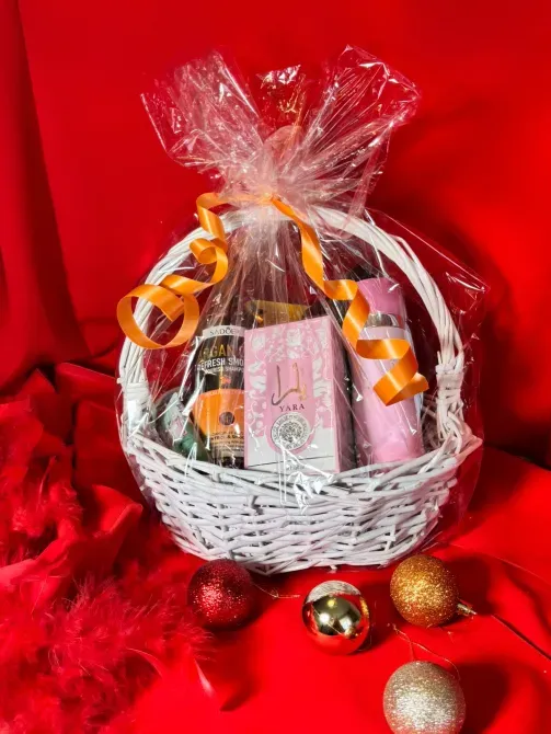 Белая корзина с косметическими средствами, обернутая пленкой и перевязанная лентой, на красном фоне