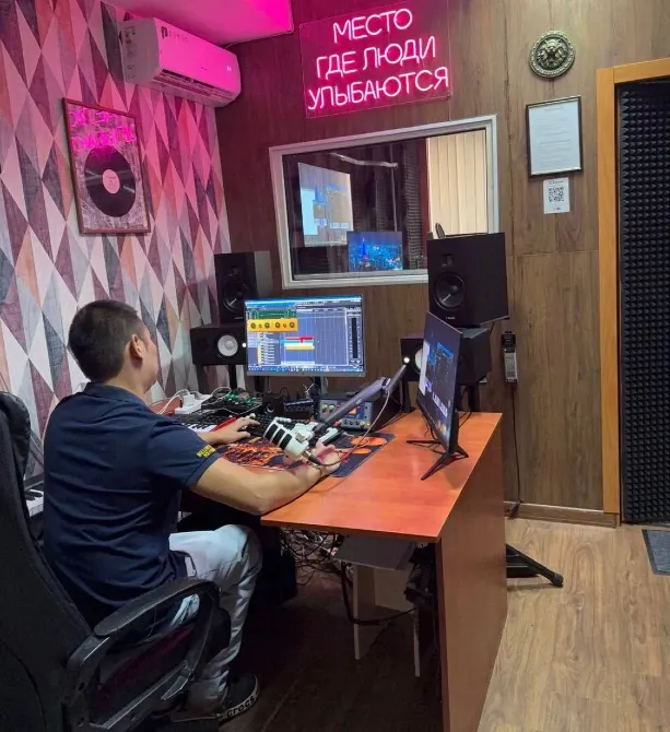 Музыкант за компьютером в студии звукозаписи с неоновыми надписями