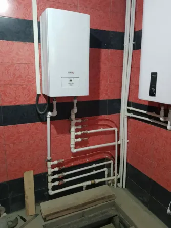 Котел на стене с водопроводными трубами и красной плиткой на стенах