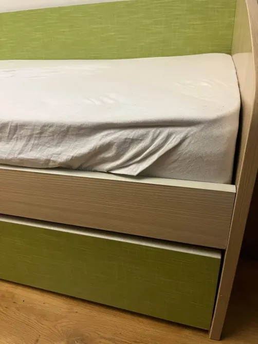 Бір адамдық төсек, шығатын бөлімімен және жасыл қаптаумен, жайлы интерьер