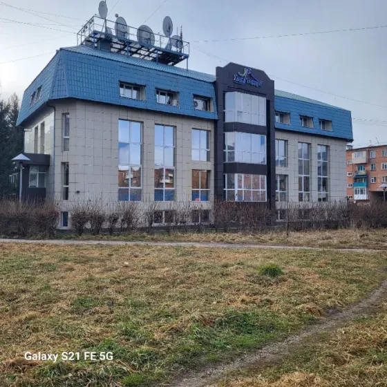 Жасыл шатырлы ғимарат және автотұрақтағы автокөліктер