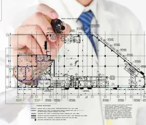 Архитектурный план здания с рабочими чертежами на фоне руки человека с ручкой