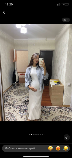 Беременная женщина в белом платье с серой рубашкой, отражающаяся в зеркале, на фоне комнаты с деревянным полом