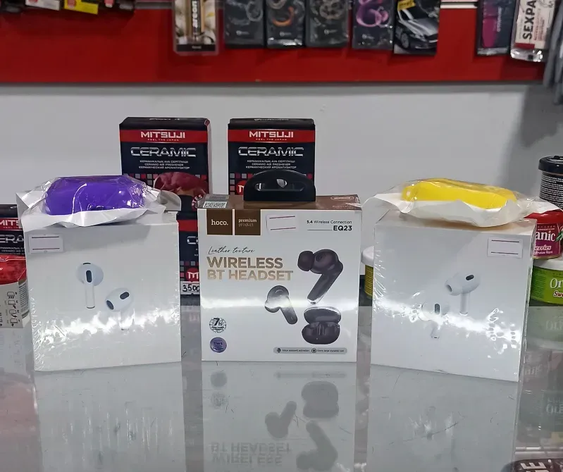 Суретте үш сымсыз құлаққаптың қаптамасы көрсетілген, олардың екеуі күлгін және сары түстермен безендірілген, ал үшіншісі — ақ, қара элементтерімен. Артқы планда Mitsuji бренді мен басқа брендтердің өнімдері орналасқан.