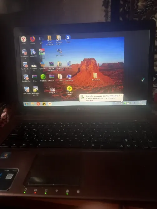 Ноутбук жұмыс үстелімен, онда қызыл таулармен фон және бағдарламалардың белгішелері көрінеді