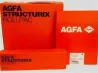 AGFA STRUCTURIX фотопленка әр түрлі форматтарда, жарқын апельсин түсті орауышпен, AGFA логотипімен.