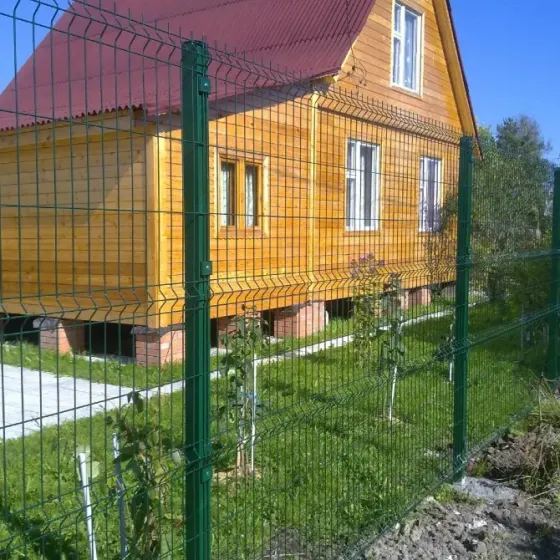 Серая металлическая ограда с вертикальными планками на фоне домов и зелени