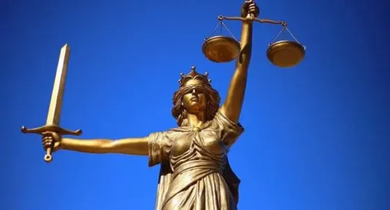 Статуя богини правосудия с мечом и весами на фоне голубого неба