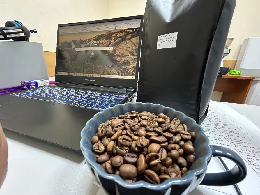 Ноутбуктың кофе дәндері бар кружкамен офис жұмыс орнының фонында