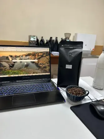 Ноутбук с открытым поисковиком Google, черный пакет с кофе и чашка с кофе на столе