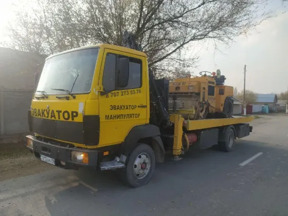Грузовой эвакуатор с манипулятором на улице, рядом с строительной техникой