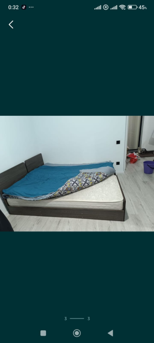 Көрпесі көтерілген және көрінетін матрасы бар кереует, жеңіл еденмен қоршалған