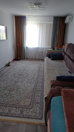 Диван, кілем және теледидармен жабдықталған бөлме, жарық терезе