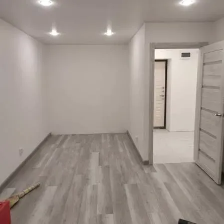 Ақ қабырғалар мен жарық еденмен безендірілген минималистикалық бөлме