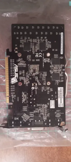 Задняя сторона видеокарты ASUS с печатной платой и компонентами на фоне прозрачного пакета