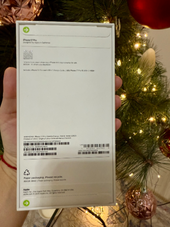 Коробка с iPhone 13 Pro в оранжевом цвете на фоне рождественской елки, украшенной шарами