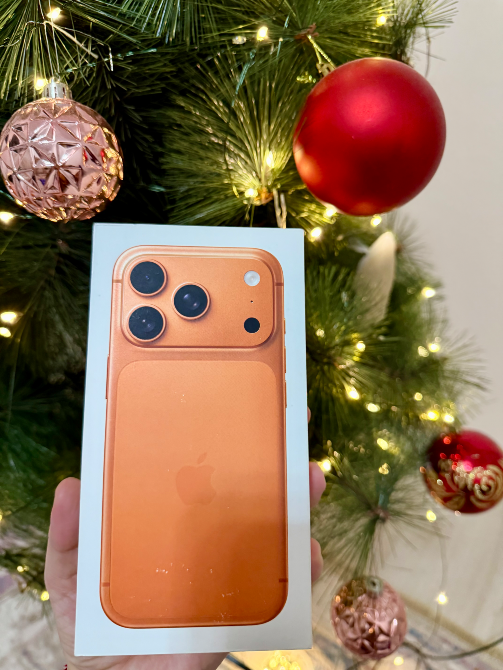 Коробка с iPhone 13 Pro в оранжевом цвете на фоне рождественской елки, украшенной шарами