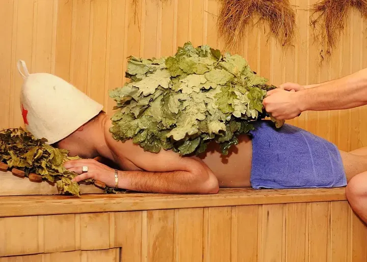 Сауна с веником и человеком, отдыхющим на скамье