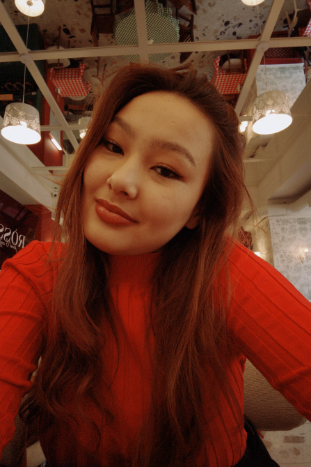 Молодая женщина с длинными волосами и красным свитером, улыбается в кафе