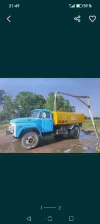 Синий грузовик с желтым кузовом, стоящий на muddy дороге, с оборудованием для выгрузки