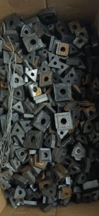 Коробка, заполненная множеством черных металлических квадратных деталей с отверстиями, на фоне проволоки