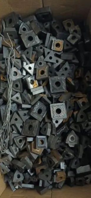 Коробка, заполненная множеством черных металлических квадратных деталей с отверстиями, на фоне проволоки