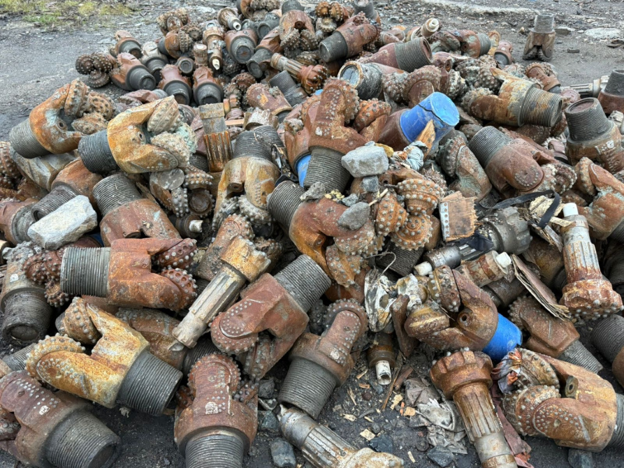 Множество ржавых буровых насадок, смешанных с другими деталями на земле