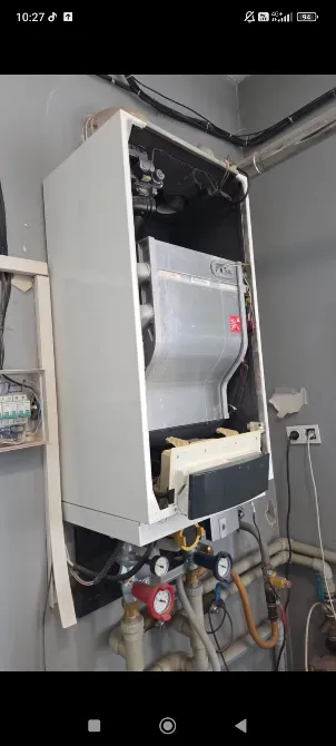 Газовый котел в разобранном состоянии с видимыми подключениями и трубами